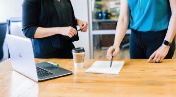 Vrouw schrijft op papier op tafel naast een laptop